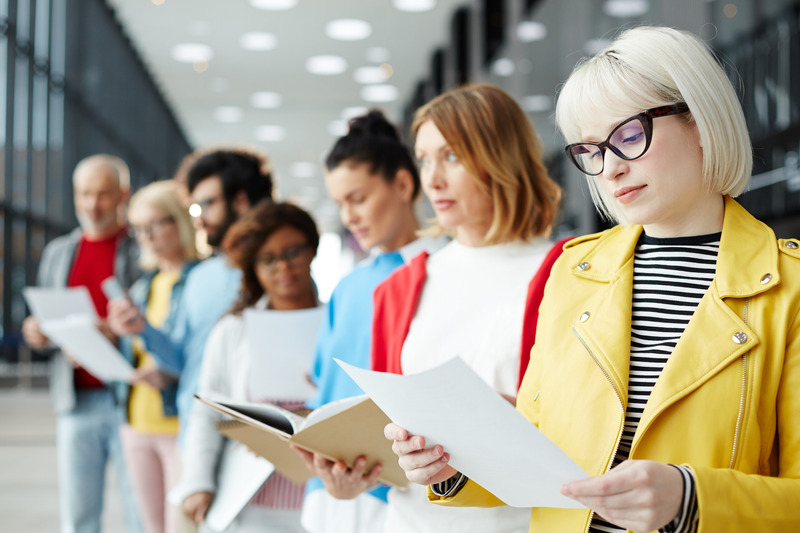 Blond Young Woman In Eyeglasses Reading Her Resume While Standing In Queue And Waiting For Her Turn For Interview